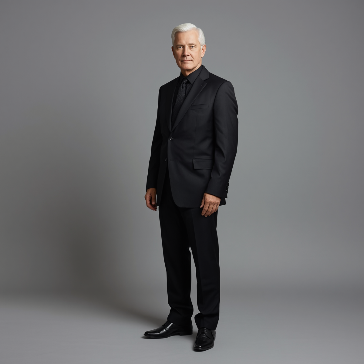 65 year old man in black suit with a grey background 